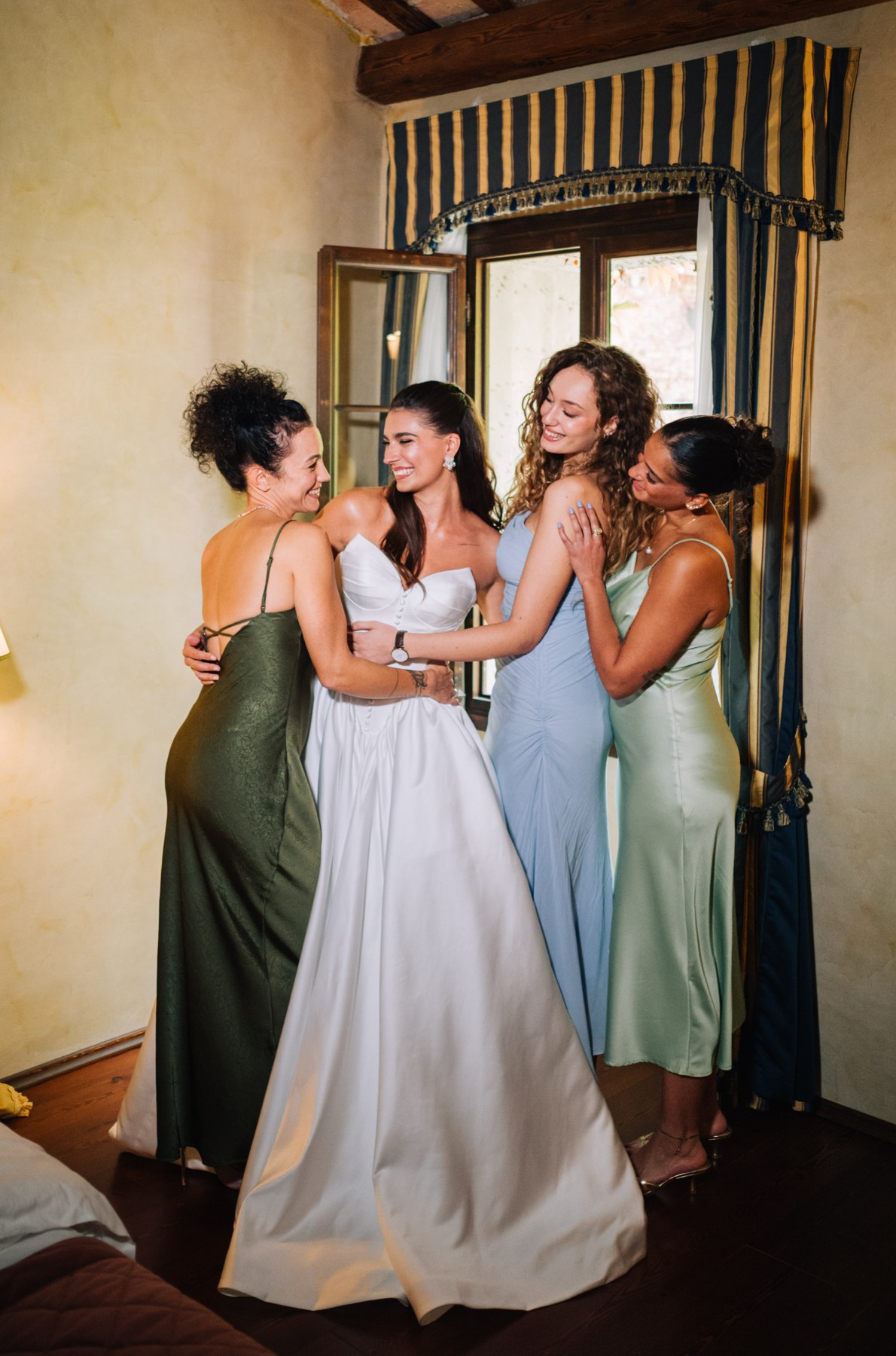 Drei Frauen in grünen und hellblauen Kleidern richten das weiße Kleid eines Models im Schlafzimmer.