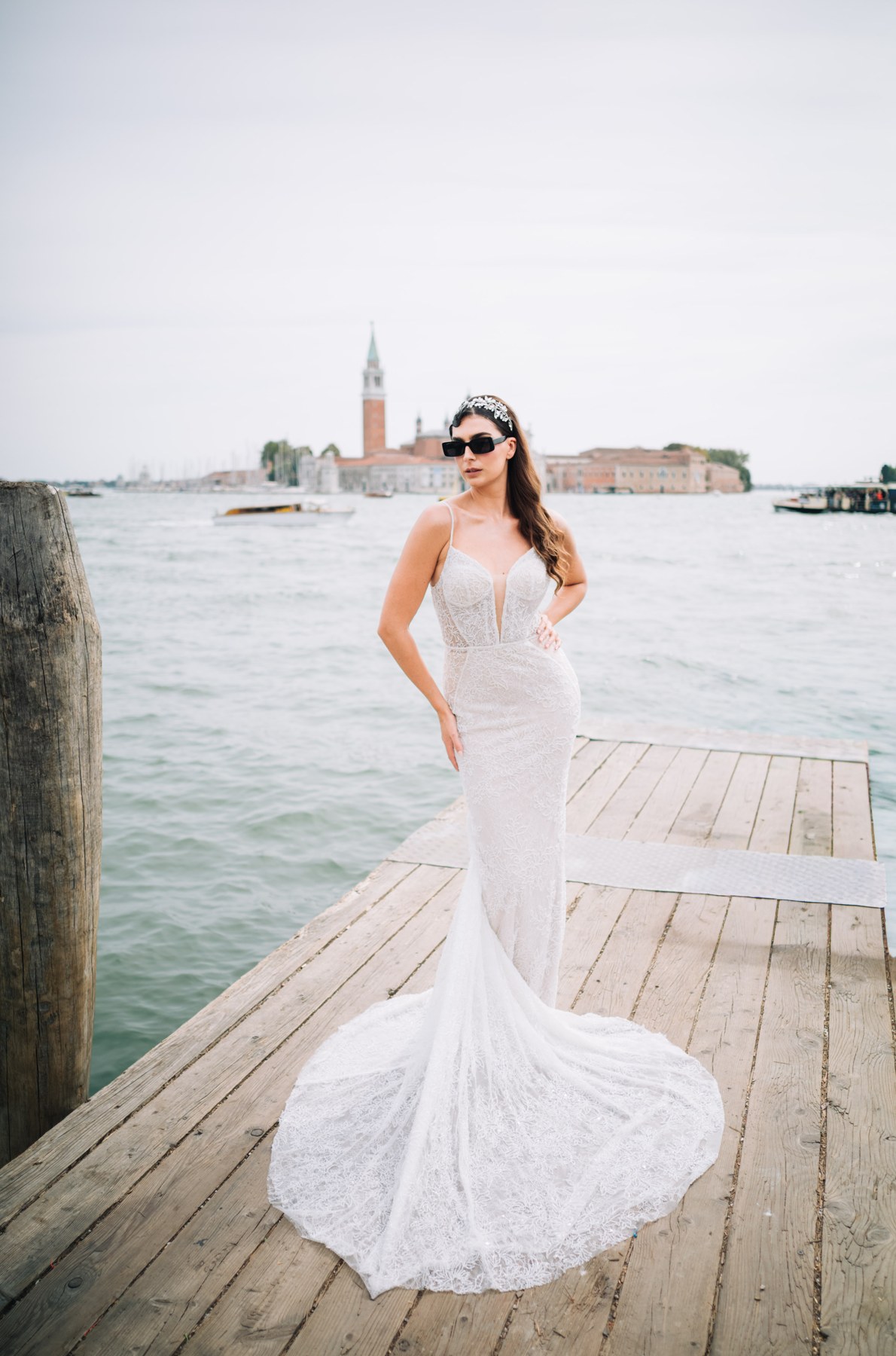 Model in einem langen weißen Kleid steht auf einem hölzernen Anleger am Wasser.