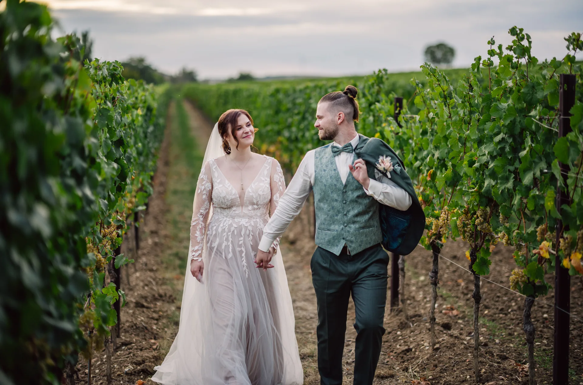 Paar in Hochzeitskleidung geht Hand in Hand zwischen Weinreben